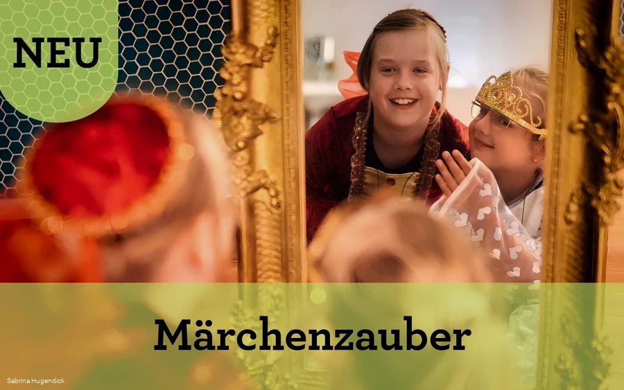 Zwei Mädchen in Prinzessinnenkleidern schauen lachend in einen golden umrandeten Spiegel